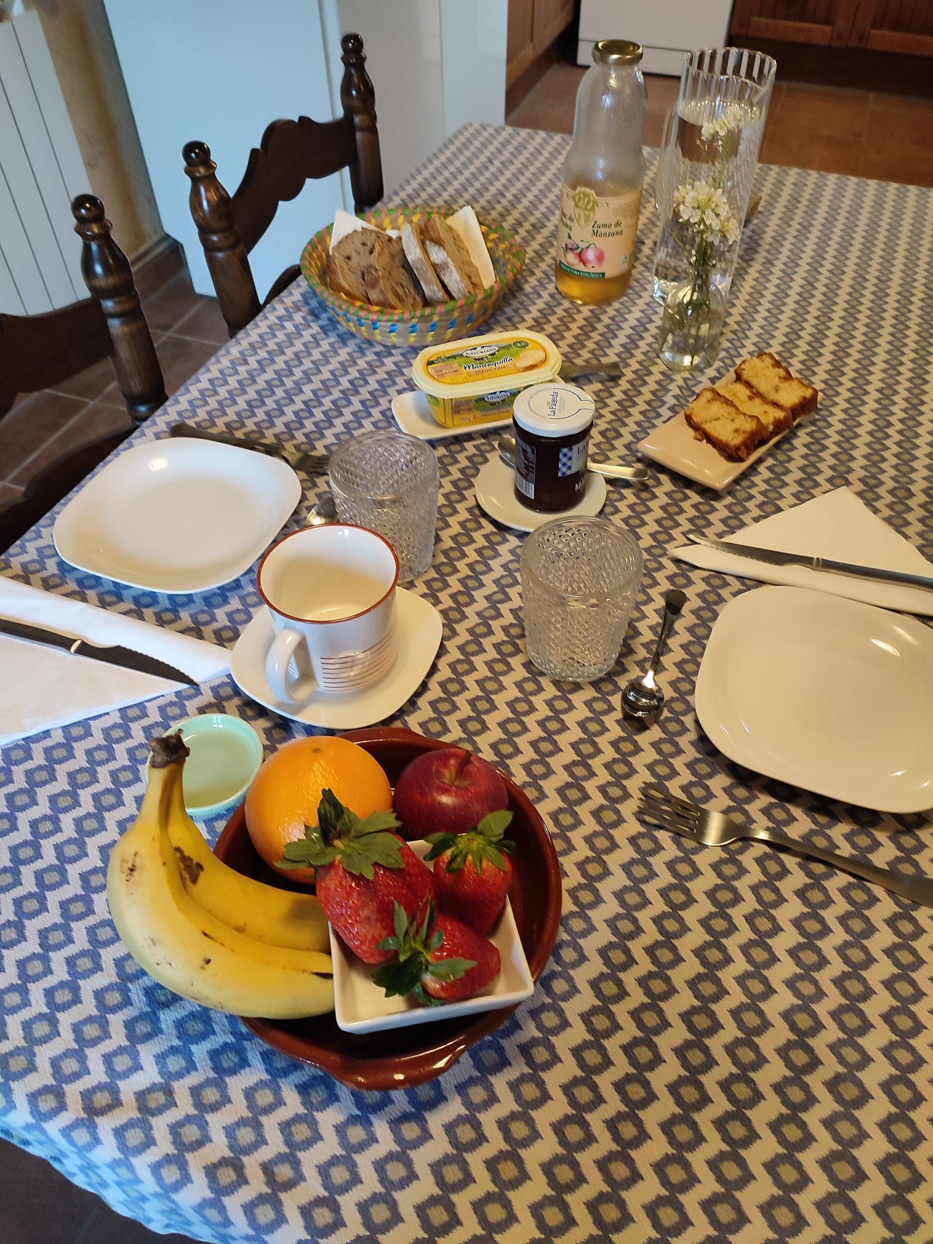 Mesa de desayuno preparada con fruta, pan y flores en un espacio cálido de convivencia